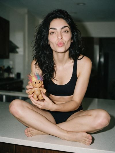 Woman in trainer bra sits cross-legged on kitchen island holding Troll doll