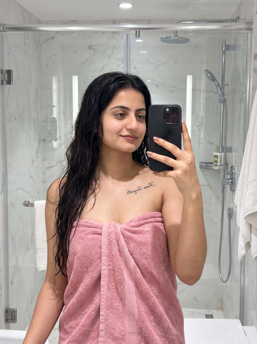 Woman with wet hair in pink towel smiles softly in marble bathroom