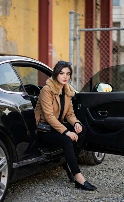 A stylish man sits on a black car door in urban setting