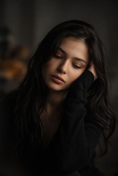 Young woman with messy hair rests head on hand in shadow