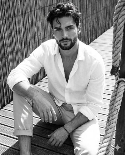 Man in linen shirt leans forward on sunlit wooden walkway