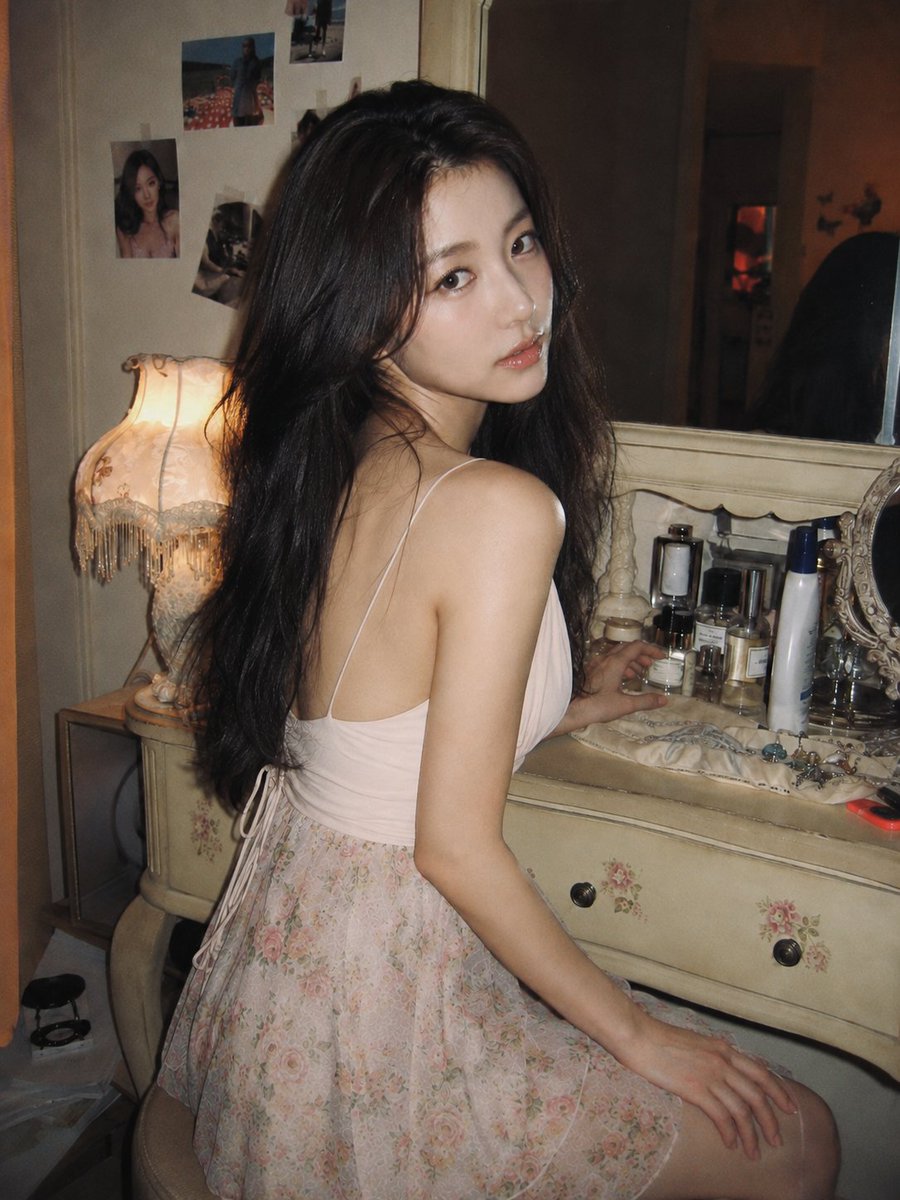 Korean woman in pink top turns from vintage vanity under warm lamp light
