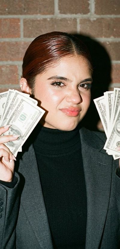 Confident woman flashes dollar bills in bright smartphone flash