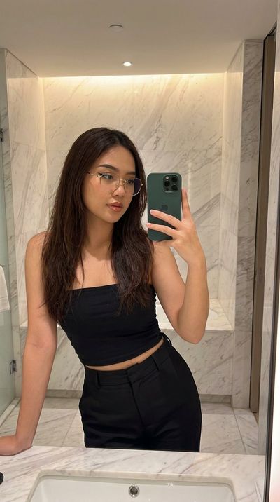 Young woman in gold glasses takes mirror selfie in marble bathroom