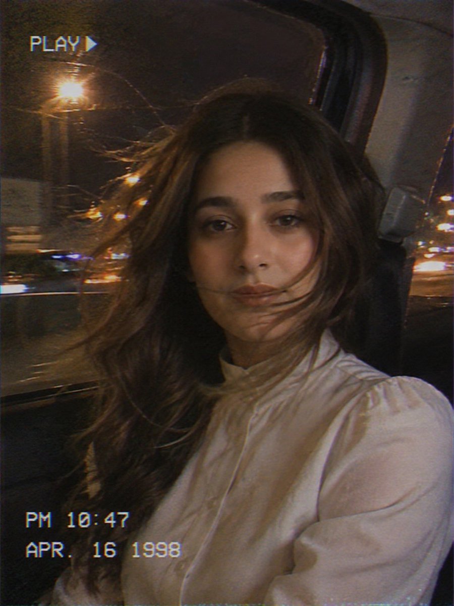 Young woman rides in backseat with city lights streaming behind her.