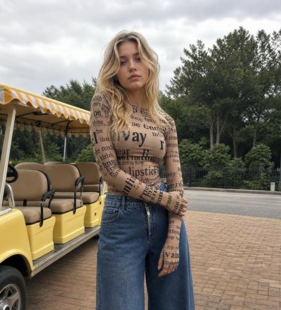 Blonde woman in typography bodysuit stands near vintage shuttle