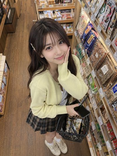 Young woman smiles in cozy grocery aisle holding basket under warm lights