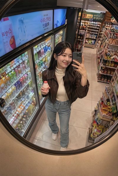 Young woman in cream turtleneck snaps selfie in Korean mart mirror
