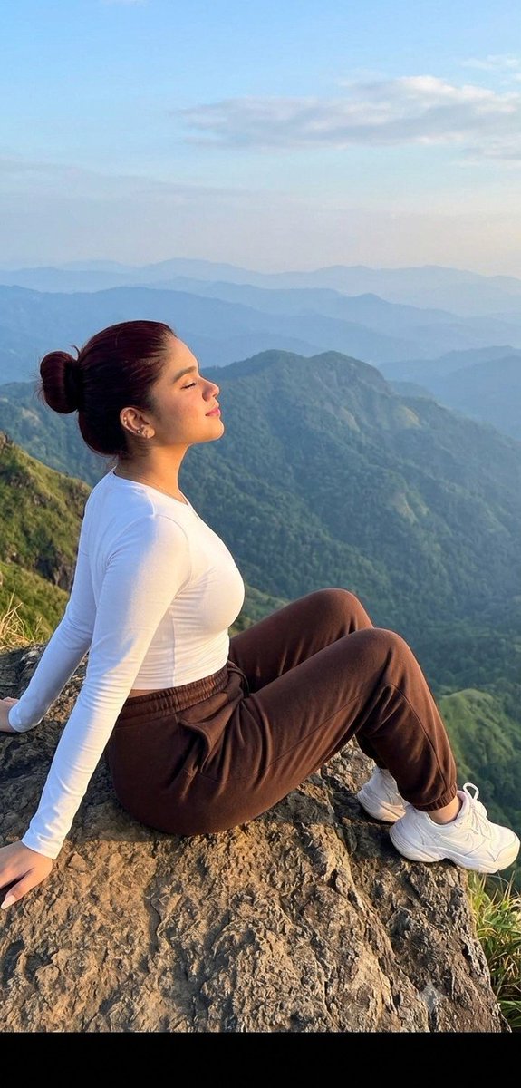 A woman sits on a cliff edge enjoying mountain views at sunrise