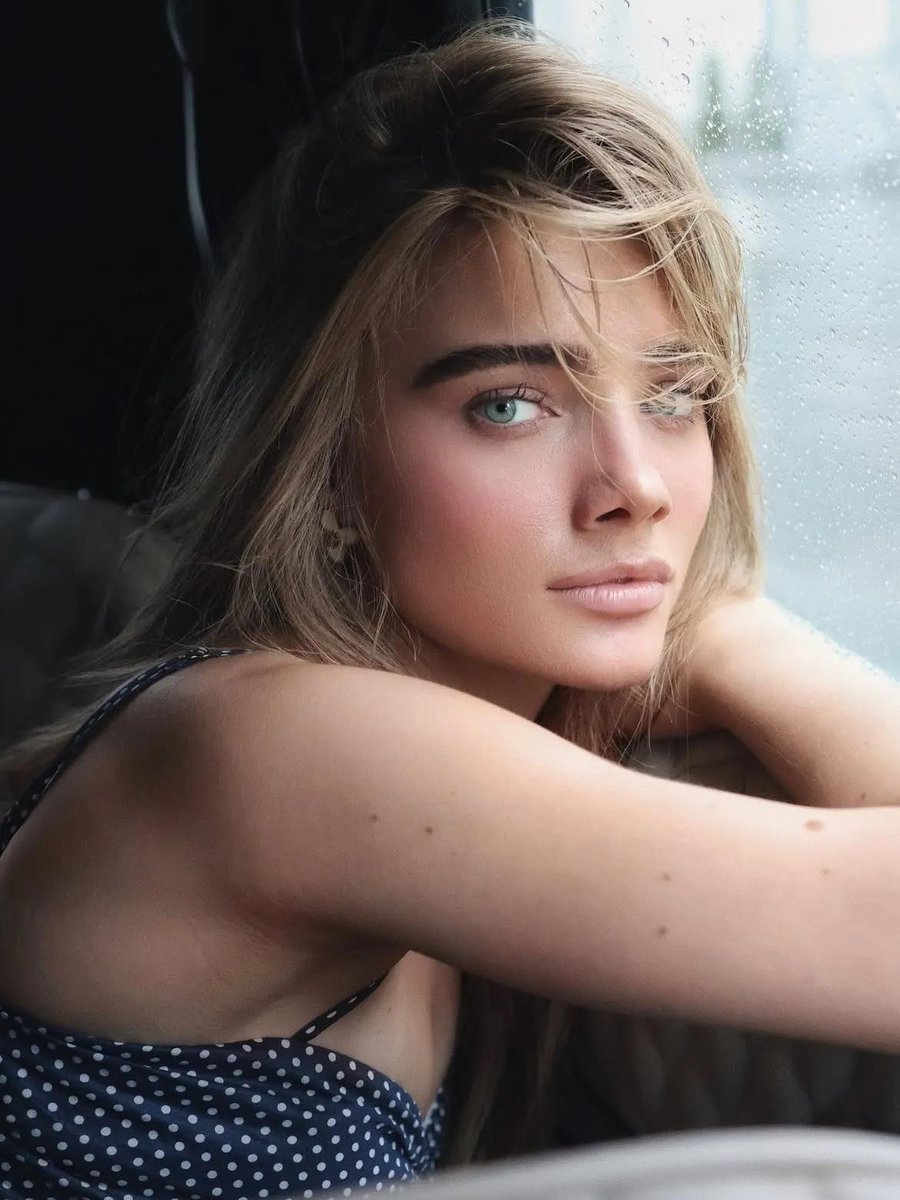 Young woman with blue-green eyes sits in vintage car looking at camera