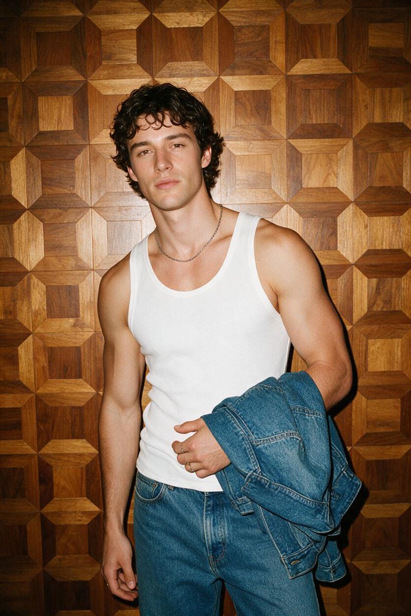 Flash-lit portrait of a man in a white tank top against a wooden wall