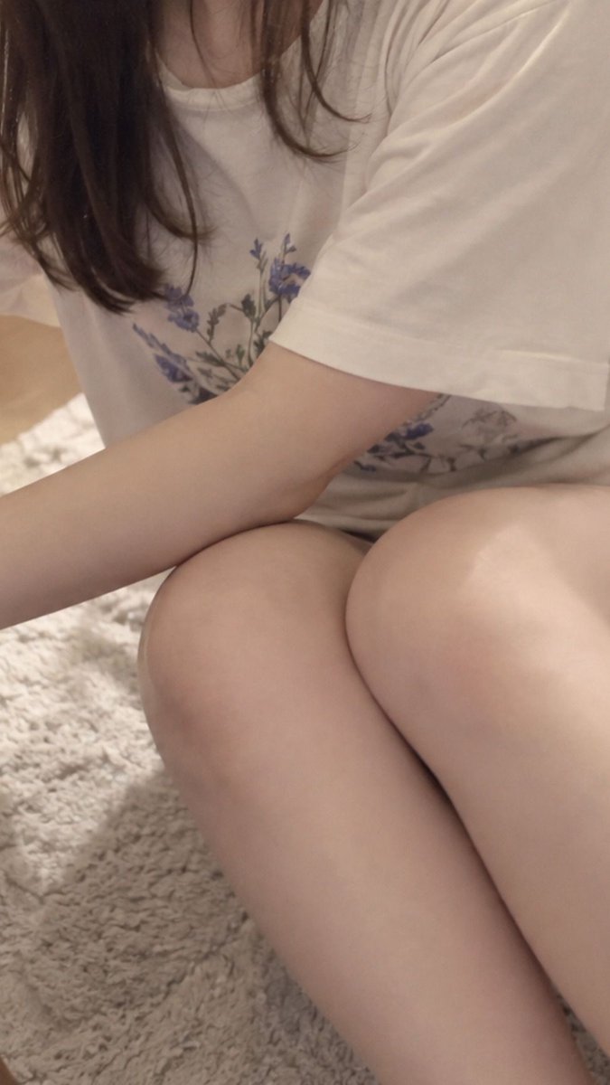 Woman in floral tee sits on rug beside bed reaching for table