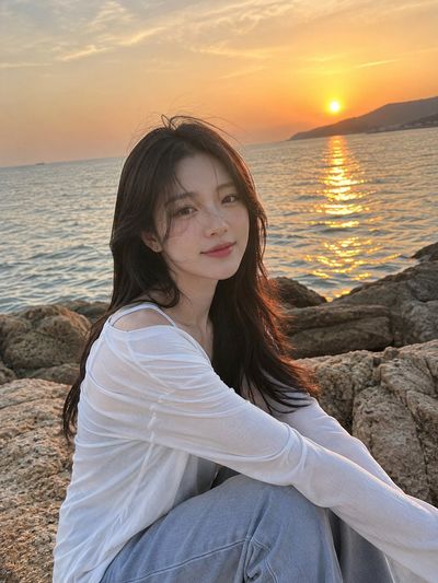 Korean man sits on coastal rock during golden sunset breeze
