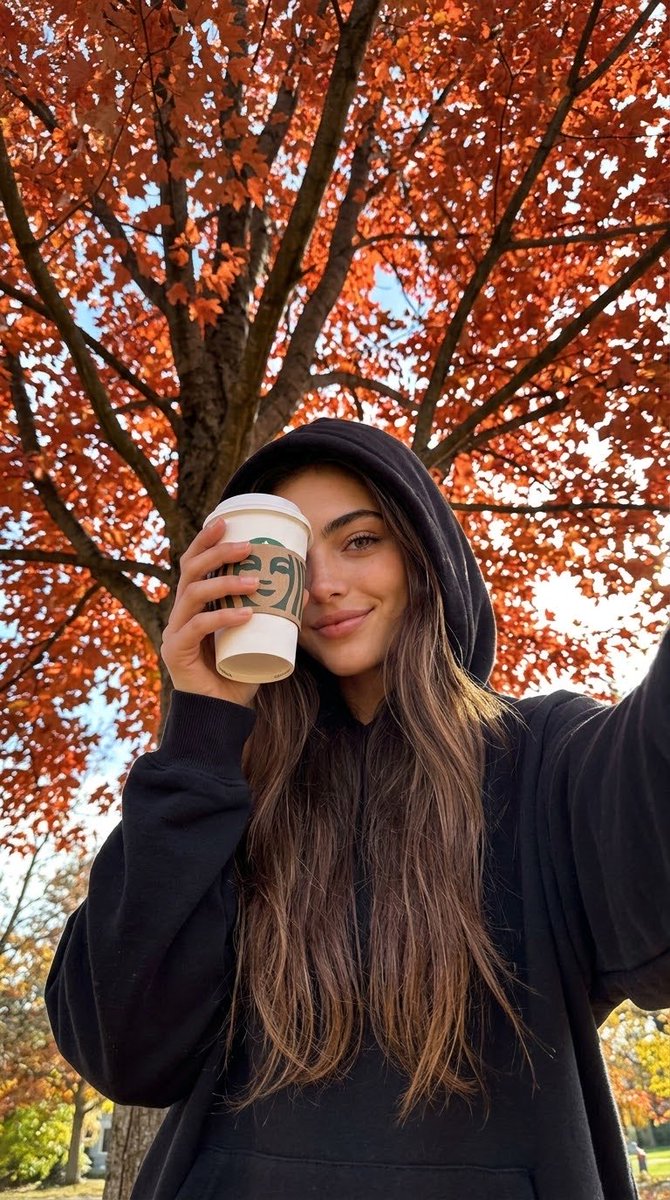 Girl in black hoodie holds coffee under autumn tree