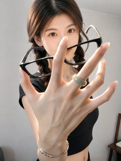 A hand holding glasses partly hides a calm face