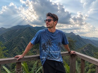 Young man with dark hair stands on mountain deck in sunlight