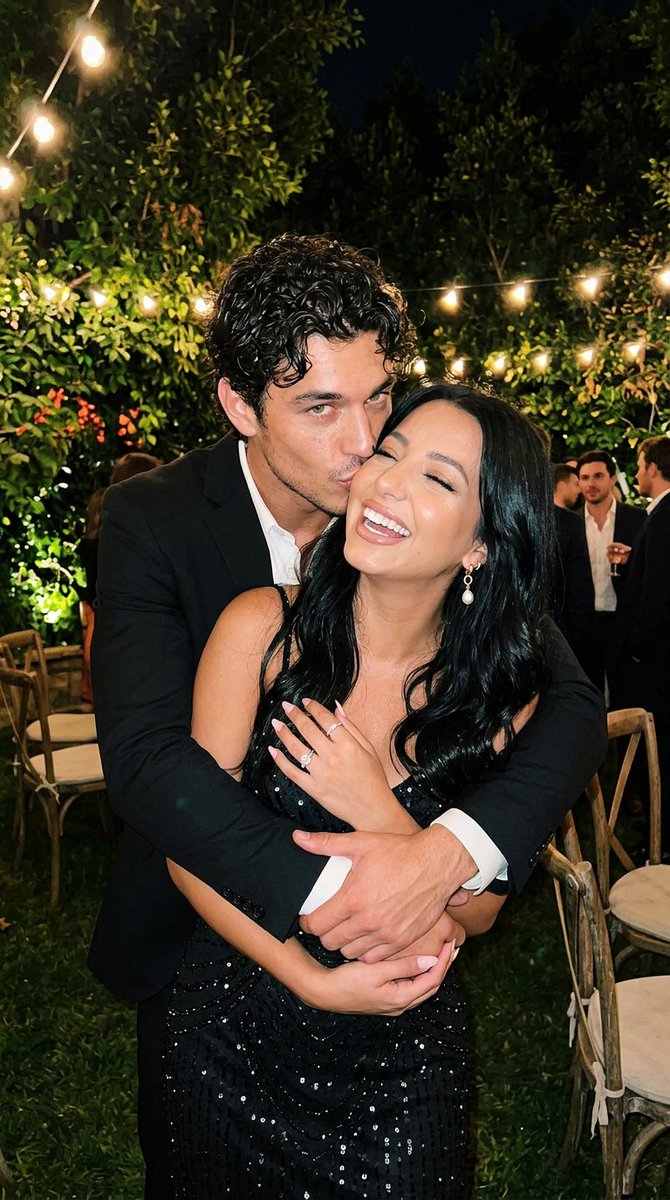 A man kisses his girlfriend's cheek at an outdoor night party
