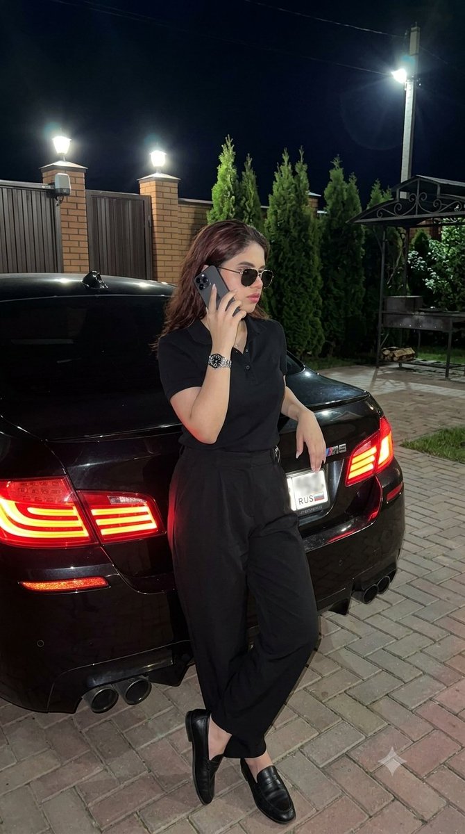 Woman leans on black BMW at night, phone to ear