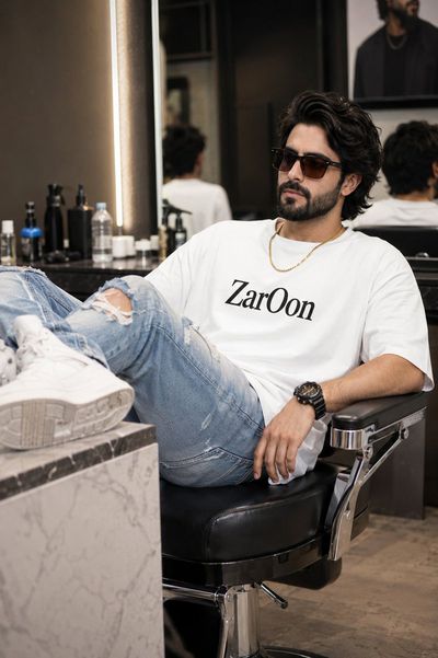 Asian man in salon chair wears oversized white tee with ripped jeans
