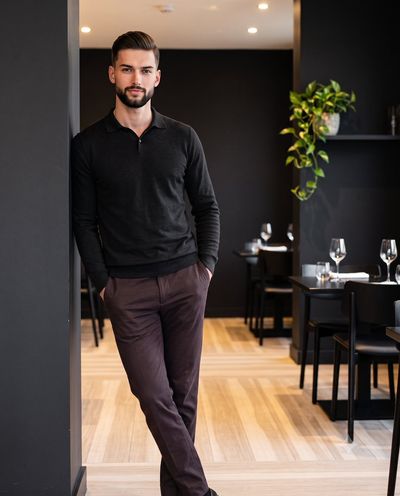 Confident man in charcoal black leans casually against a column