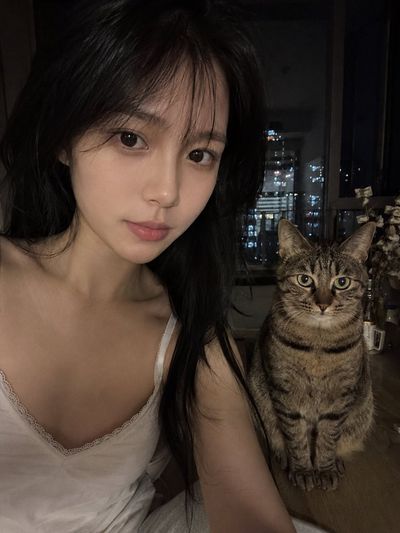 Young woman in white lace top shares quiet night with tabby cat