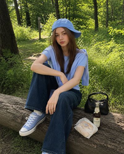 Young girl in pastel blue sits on a log in a sunlit forest.