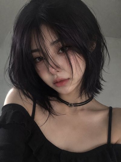 A woman with dark bob hair holds a daisy to her lips