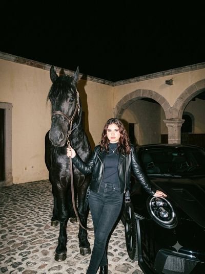 Woman Leans on Black Porsche with Friesian Horse in Flash Photo