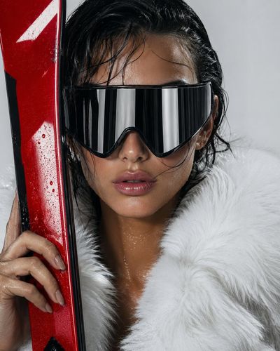 A woman in futuristic goggles holds a red ski against white fur.