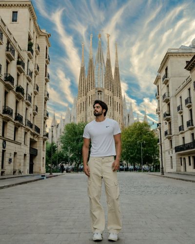 A traveler stands before Sagrada Família under dramatic clouds.