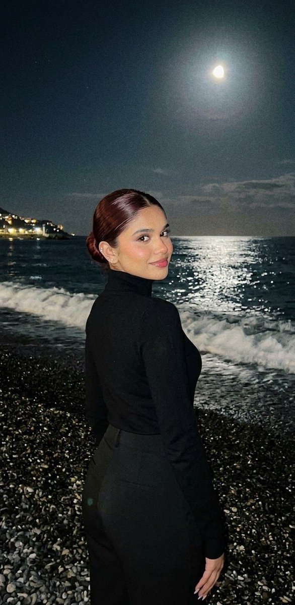 A woman in a zebra top gazes back under a full moon on the beach