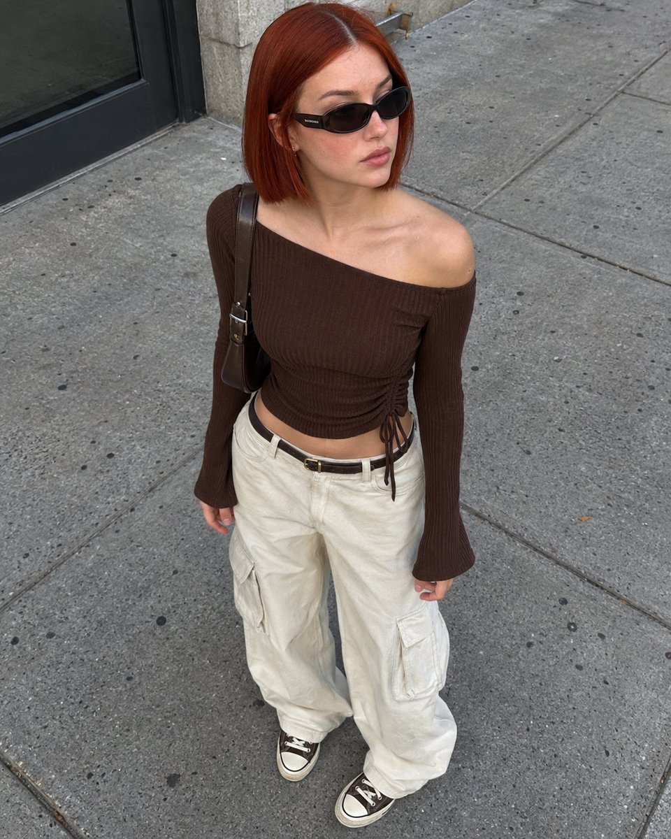 Auburn-haired woman in brown top stands on sunlit city sidewalk