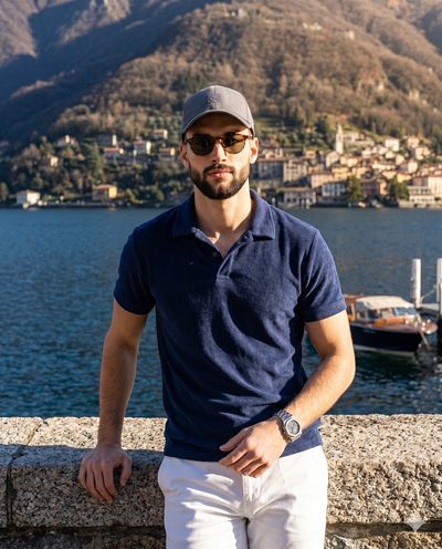 Man in navy polo leans on granite wall by Lake Como