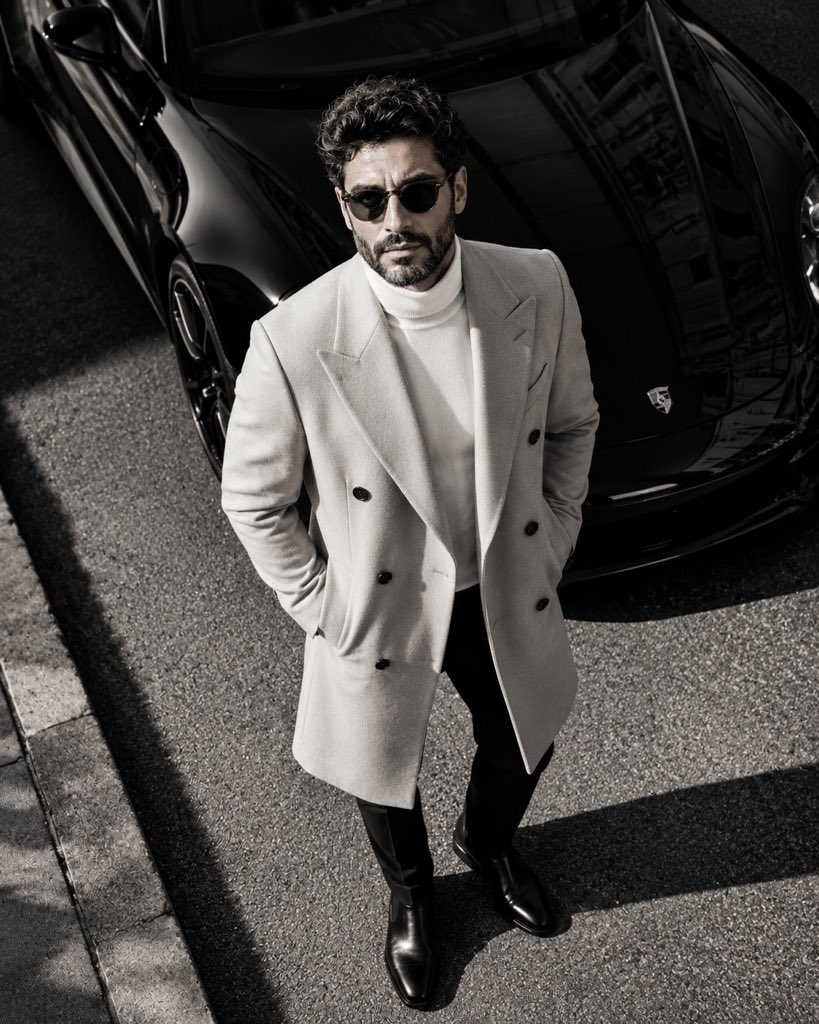 A confident man in an overcoat stands by a luxury car