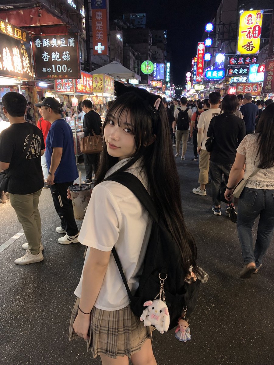 A young girl in a cat headband explores a neon-lit night market.