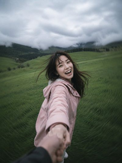 Couple spins laughing in grassy field under moody clouds