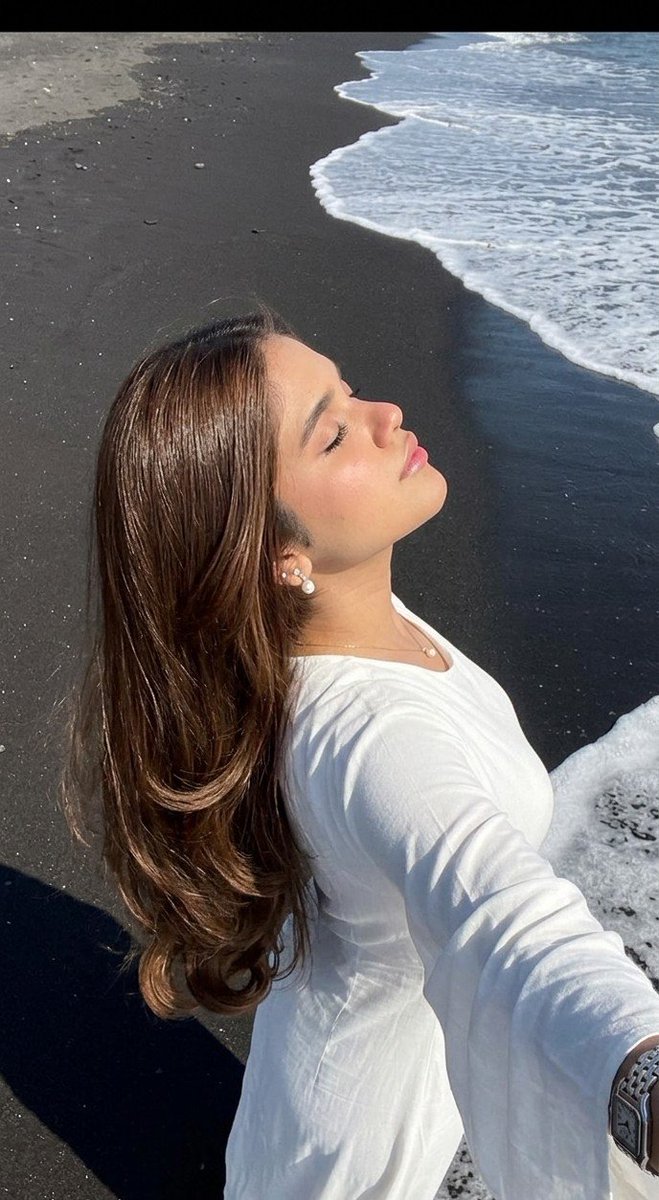 Woman in white dress stands on black volcanic beach sand