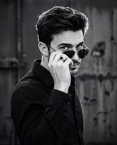 A confident man grips his aviator sunglasses in dramatic monochrome