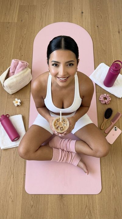 Woman sits cross-legged on pink yoga mat holding iced coffee
