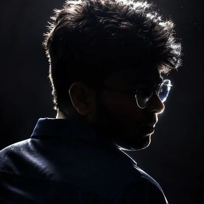 A young man's shadowed profile highlights sharp jawline and rim-lit glasses.