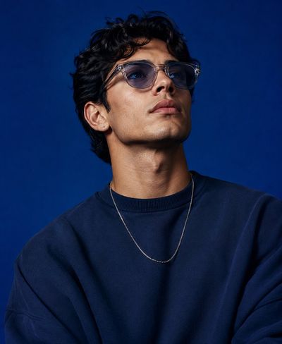 A model in oversized knitwear gazes upward against deep cobalt backdrop