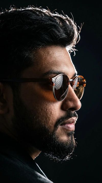 Young man's profile emerges from darkness with rim-lit sunglasses