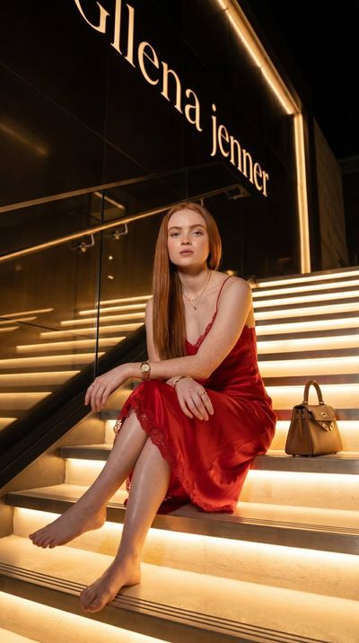 Sadie Sink sits on a glowing staircase in red satin