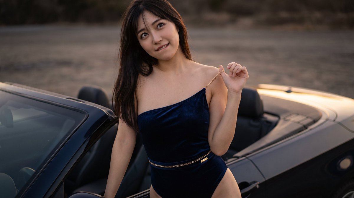 Woman laughs beside black car in golden hour light