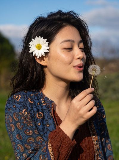 Woman with closed eyes blows dandelion seeds in sunlit field