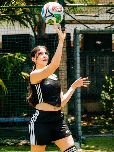 Athletic woman tosses a spinning volleyball under bright tropical sunlight.