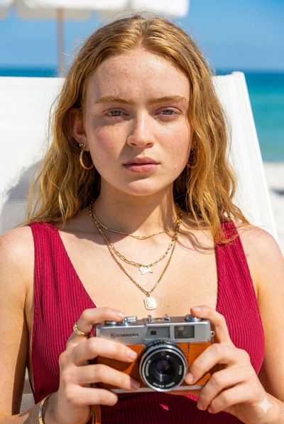 A platinum blonde lounges on white sand in crimson swimwear