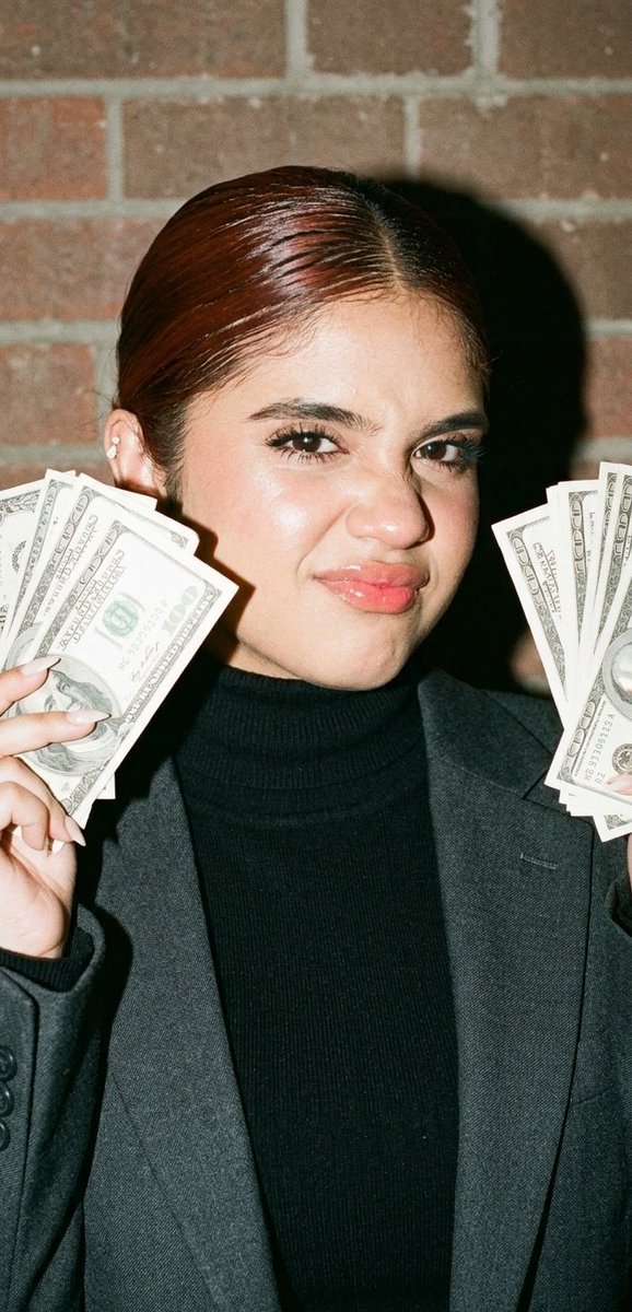 Confident woman flashes dollar bills in bright smartphone flash