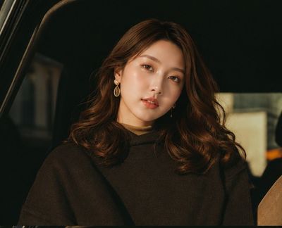 East Asian woman in gold earrings poses inside luxury car at golden hour