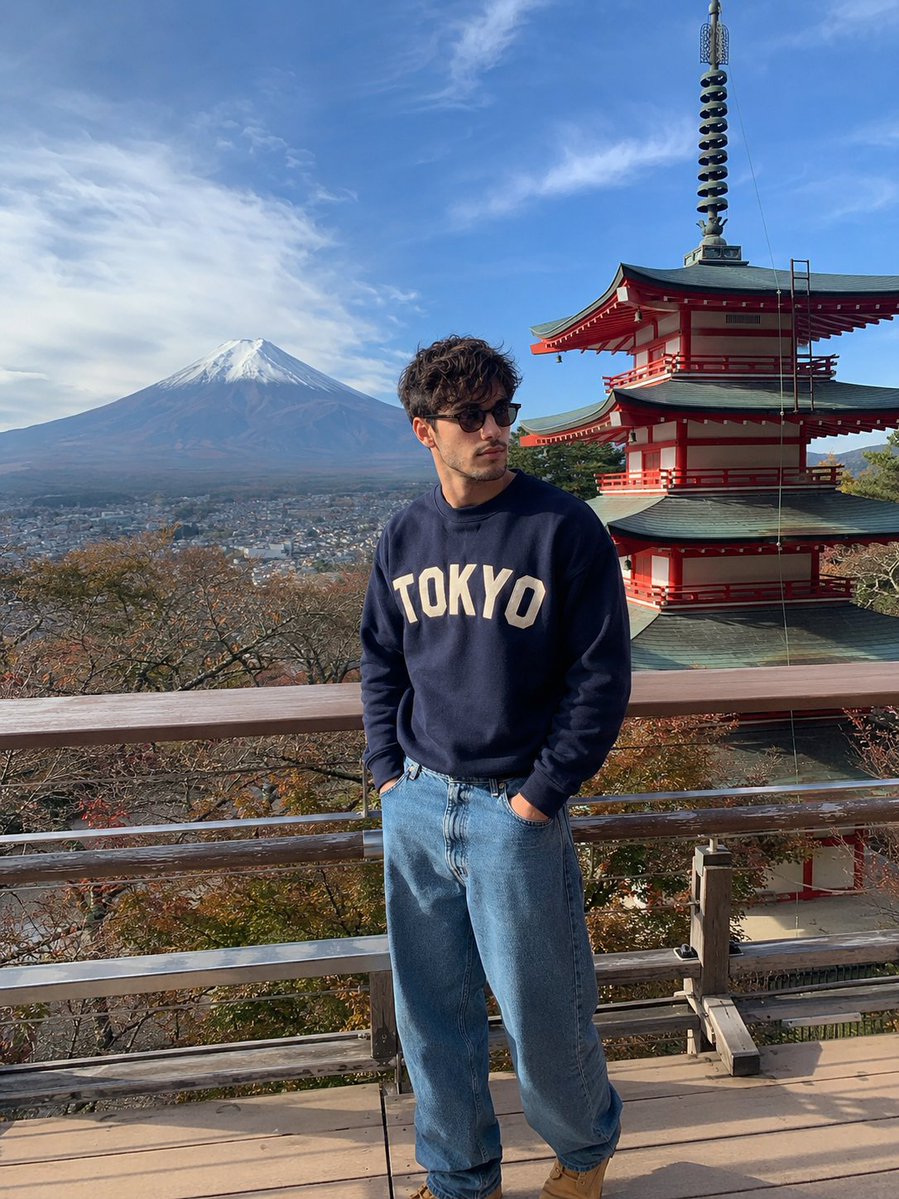 A man in navy sweater views Mount Fuji from a wooden deck